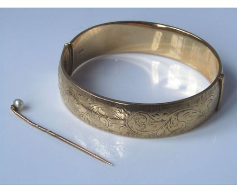 An early 20th Century 9k gold bangle with chased floral decoration 35.1g together with a boxed yellow metal tie pin with pear