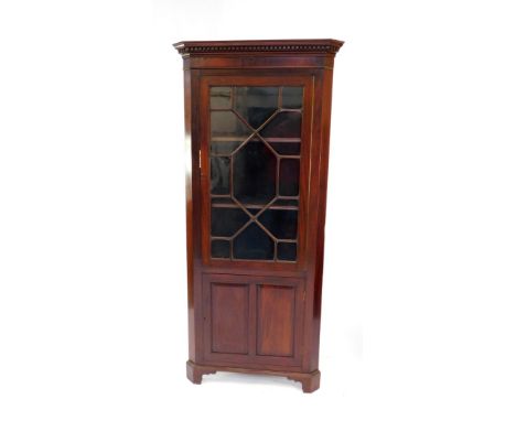 An Edwardian mahogany corner cabinet, the dentil moulded pediment over a glazed door opening to reveal two shelves, above a c