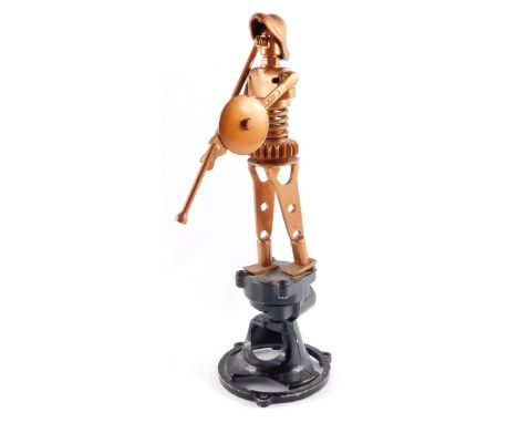 An Abstract gold sprayed metal figure of a soldier, formed from various tools and other mechanical parts, raised on a black b