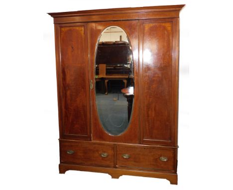 An Edwardian mahogany and inlaid double wardrobe, the central door inset bevelled oval glass opening to reveal hanging rails 