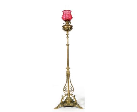 A Victorian brass standard lamp with pierced column on scroll cast base with ruby moulded shade, height 162cm