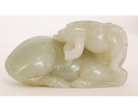 A Chinese pale celadon jade carving of a recumbent goat or ram with its head turned back holding a branch of  lingzhi fungus 