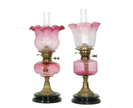 Two Victorian ruby oil lamps and shades each with conforming reservoirs on circular black glazed bases. (2)