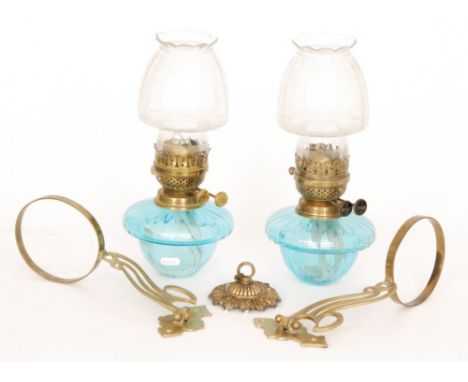 A pair of Art Nouveau style 20th Century oil lamps and shades with light blue reservoirs and brass arm brackets. (2)