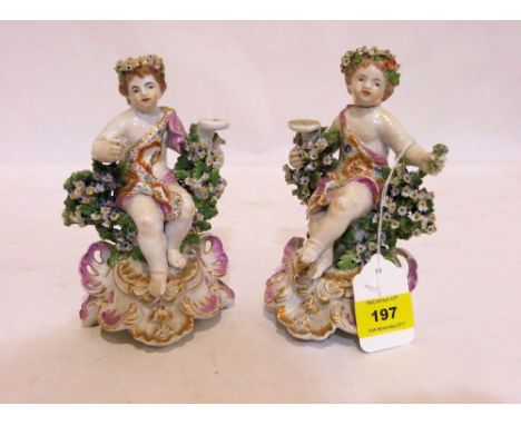 A pair of Dresden type figures of putti, gilded and richly decorated in colours with encrustations of applied flowers, on scr