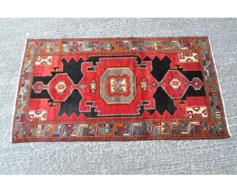 A vintage floor rug with a geometric pattern in shades of red, black and orange, 130cm x 220cm
