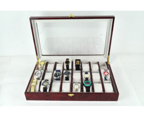 A modern watch collection box with clear top, containing a selection of wristwatches, including a Swatch, Nautica, Guess, Fos