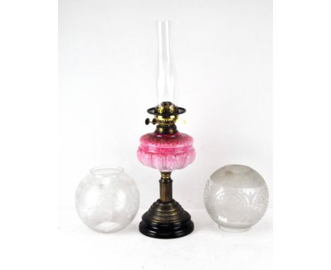 A late Victorian oil lamp, with a pink glass well, the brass stand in the form of a column on a circular ceramic base, togeth