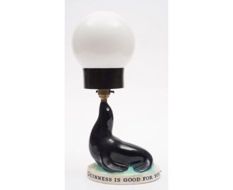 A Carlton Ware Guinness Sealion lamp with associated shade:, raised on a black glazed seal on an oval base, black printed bac