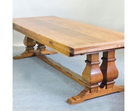 An unusually large light oak refectory style draw leaf dining table, having a plank top, on twin end supports, united by a ce