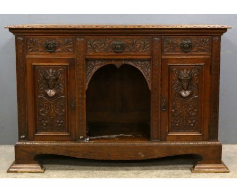 Oak dresser base, with three drawers and two cupboard doors carved with masks and scrolling foliage, on stepped bracket feet,