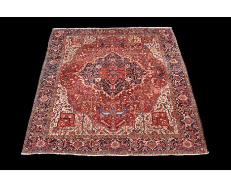 A Heriz carpet, decorated overall with stylised foliate motifs, the madder and navy medallions within a polychrome decorated 