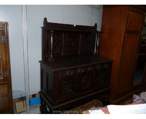 A dark Oak early 20th c. Sideboard having carved details, upper shelf with turned supports standing on substantial turned leg