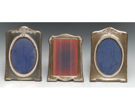 A pair of George V silver shaped arched rectangular easel photograph frames, each embossed in the Neo-Classical taste with a 