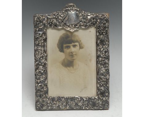 An Edwardian silver rectangular easel photograph frame, profusely embossed with scrolling foliage, vacant cartouche cresting,