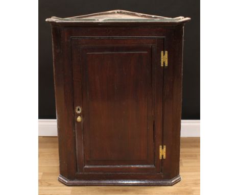 A George III oak wall hanging corner cabinet, moulded cornice above a raised and fielded panel door enclosing a shelf, brass 