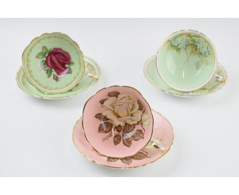 A trio of Paragon cups and saucers to include a green coloured duo with pink rose decoration to interior, signed 'R Johnson',