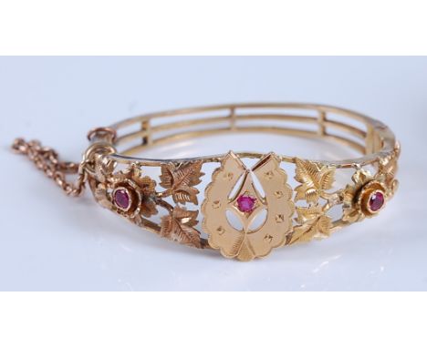 A late Victorian yellow metal hinged bangle, the bangle having engraved openwork detail of a horseshoe motif with flowers and