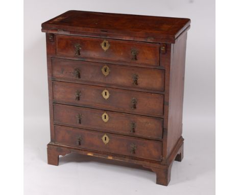 An antique walnut bachelors chest of small proportions, having a fold-over top with cross and featherbanding over four long g