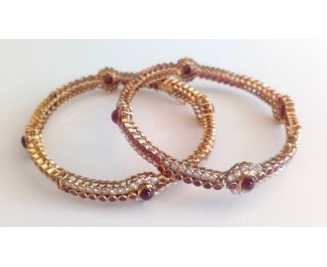 A pair of yellow metal, ruby and diamond hinged bangles, each bangle having four oval cabochon cut, sixty-four faceted rubies