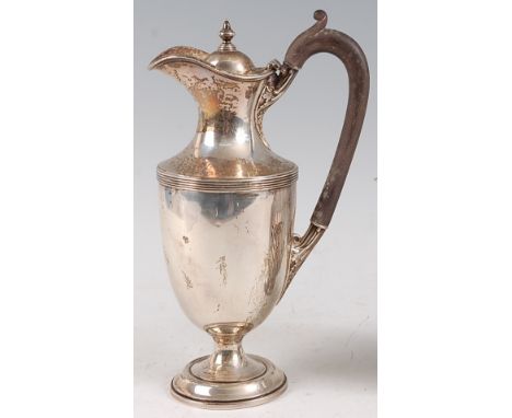 A George V silver hot water jug, the cover having acorn finial, ebonised handle with acanthus leaf terminals, the whole on ci