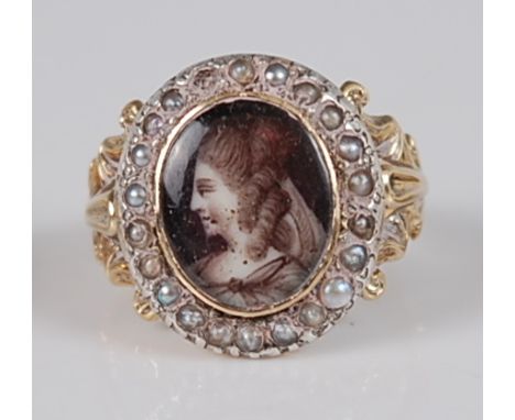 A George III yellow metal and seed pearl mourning ring, centre set with a monochrome painted profile portrait of a maiden, 11
