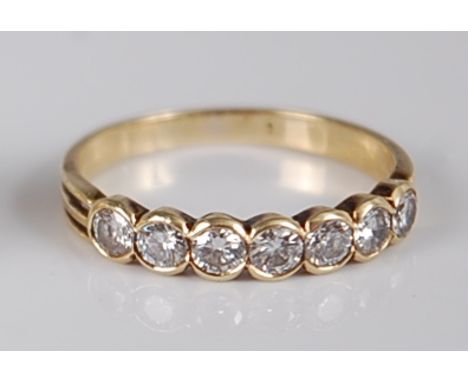 A yellow metal diamond half hoop ring, arranged as seven illusion set brilliant cut diamonds in a line setting, total diamond