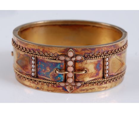 A late Victorian yellow metal hinged oval bangle, the bangle having an engraved buckle detail to the front with ten 2.3mm see