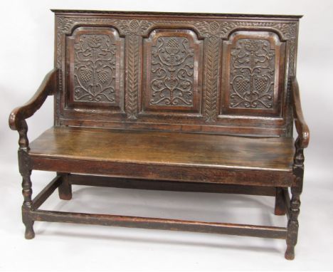 A 17thC oak settle, the triple panel back carved with fruits and leaves, solid seat, raised on turned supports united by stre