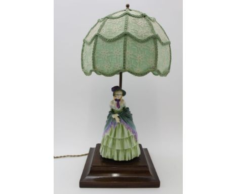 An early to mid-20th century table lamp, the polished wood base mounted with a porcelain figure of a Victorian young lady (po