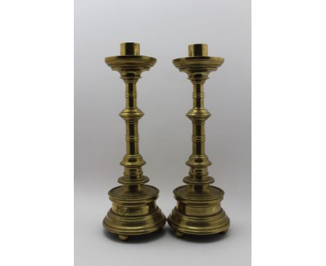 A pair of German Gothic design brass candlesticks, ring knop stems on weighted bases, each raised upon three bun feet, 50cm h