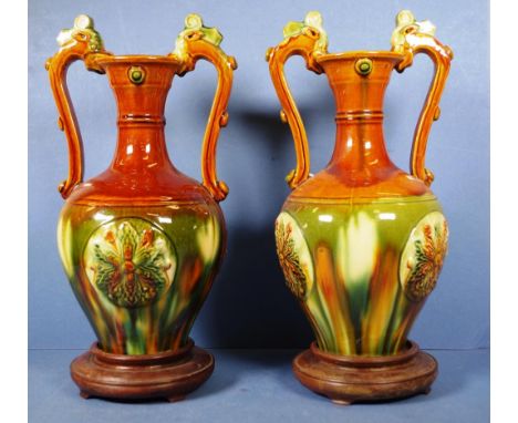 Pair Chinese ceramic dual handled ewers each with embossed decoration, on wood stands. Height 35cm approx (each).