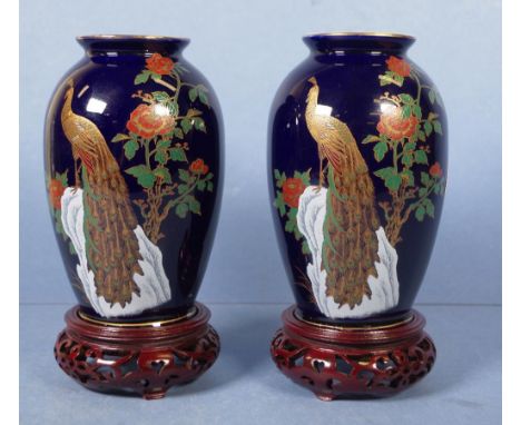 Pair Chinese ceramic vases on stands each with peacock decoration on blue ground, on carved wood stands. Height 20cm approx (