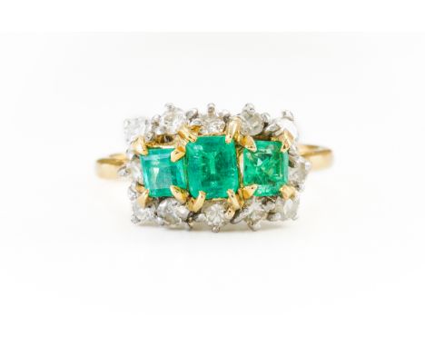 AN EMERALD AND DIAMOND RINGWith three central emerald cut emeralds surrounded by round brilliant diamonds, all claw set in go