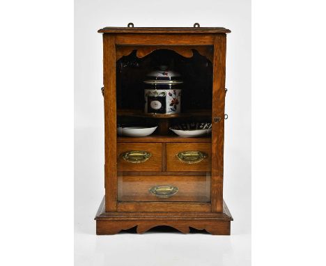 An early 20th century oak smoker's cabinet, the glazed door enclosing three shelves and ceramic tobacco jar and two dishes, h