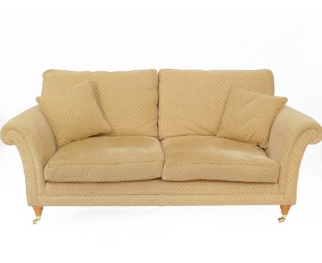 A Parker Knoll two seater sofa, upholstered in a fawn repeating floral fabric, raised on turned legs, brass capped on castors