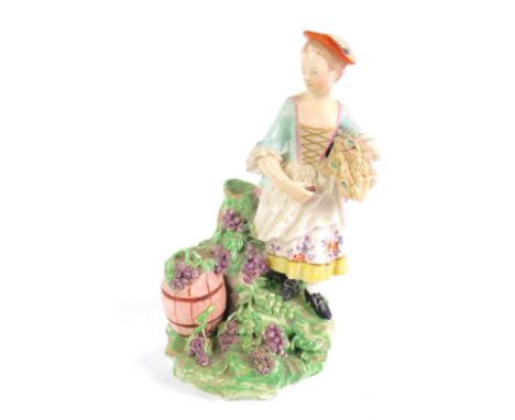 A late 18thC Derby porcelain figure of a lady, modelled standing holding corn under her arm, aside a barrel and flowing grape