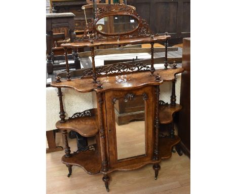 A Victorian walnut four-tier whatnot, with central cupboard behind mirror door, galleried top with further oval mirror panel 