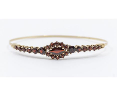 A garnet set 9ct gold bangle, the top claw set with marquise cut to the centre within a border of round cut stones, width app