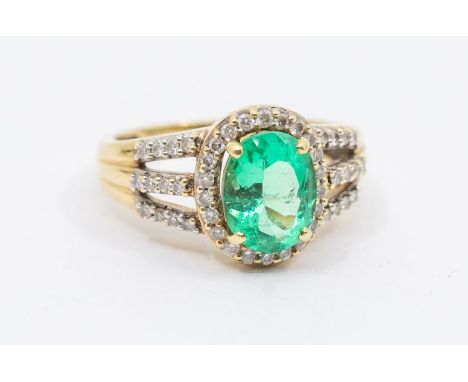 An emerald and diamond 18ct gold ring, comprising a claw set oval cut emerald to the centre approx 7 x 9mm, within a border o