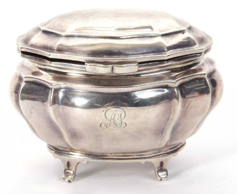 An Edwardian silver oval caddy of plain serpentine form, having a hinged lid and supported on four splay feet, engraved to th