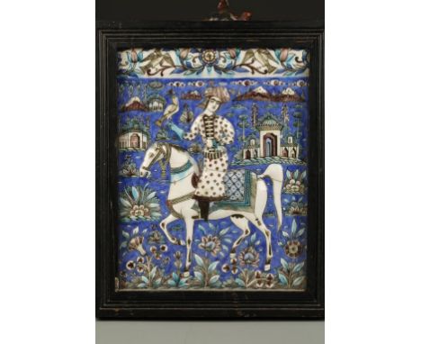 A QAJAR POTTERY MOULDED TILE showing a hawker in a landscape with buildings beyond, the top with a foliate band, 19th century