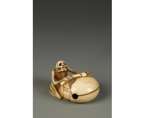 A JAPANESE IVORY SKELETON NETSUKE, the figure seated beside a gong, circa 1900, signed underneath, 2" long