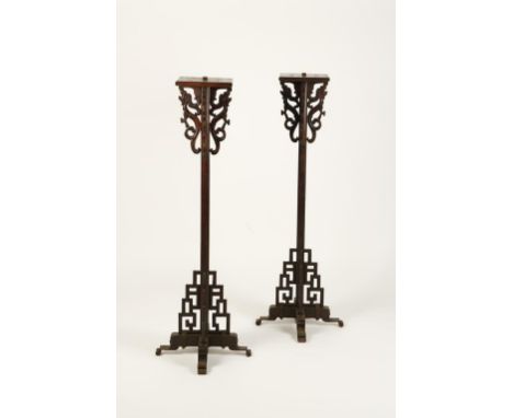 A PAIR OF CHINESE WOOD CANDLESTANDS of geometric form, the square tops above four dragon scrolls, on reeded stems with scroll