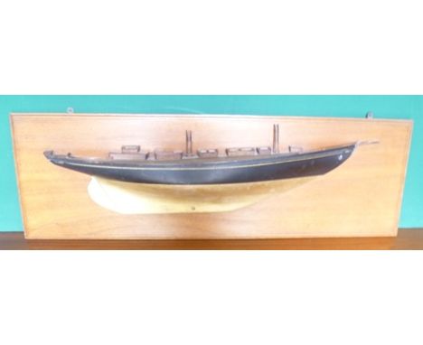 A HALF HULL MODEL YACHT, ebonised and gilded, with plank effect deck and broken masts, laid on a mahogany panel, 32.5cm x 101