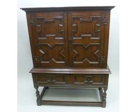 AN ELIZABETHAN DESIGN OAK CABINET ON STAND fitted with two moulded panel doors over single drawer to base, decorative metal f