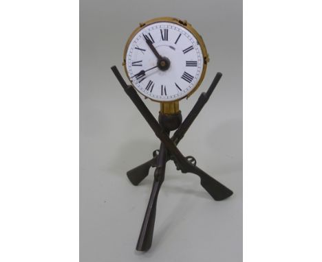 A TABLE CLOCK FORMED AS A GILDED DRUM balanced on a crossed frame of three rifles, white enamel dial with Roman numerals, 22c