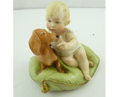 A CAPO-DI-MONTE PORCELAIN FIGURE of a fair haired child playing with a Dachshund, on green cushion, 9cm high x 10cm wide 