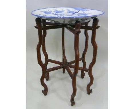 A JAPANESE OCCASIONAL TABLE, comprising a blue and white painted charger on a folding wooden stand, the charger decorated wit