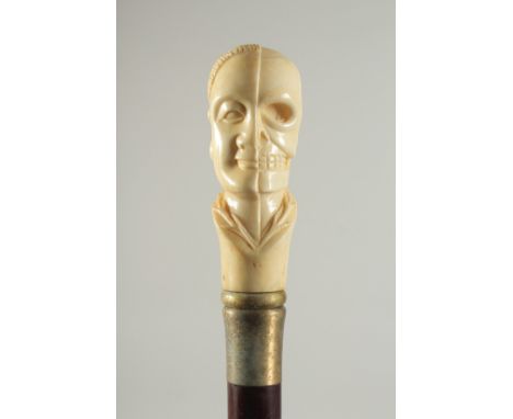 A CARVED BONE HANDLE WALKING STICK "HEAD &amp; SKULL". 2ft 11ins long.